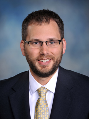 Male with black blazer, white collared shirt and yellow and grey neck tie.