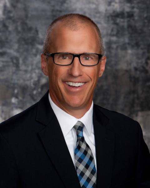 male with black blazer, white collared shirt and black, blue, and grey neck tie.