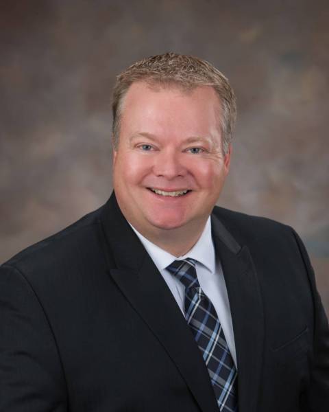 male with black blazer, white collared shirt and navy and light blue neck tie.