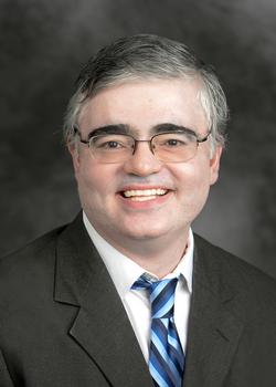 male with charcoal blazer, white collared shirt, with blue and navy striped neck tie.